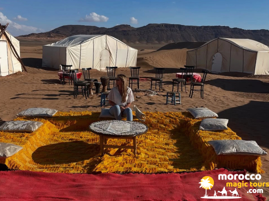 A traveler sitting on comfortable yellow outdoor cushions at a traditional desert camp lounge surrounded by white tents.