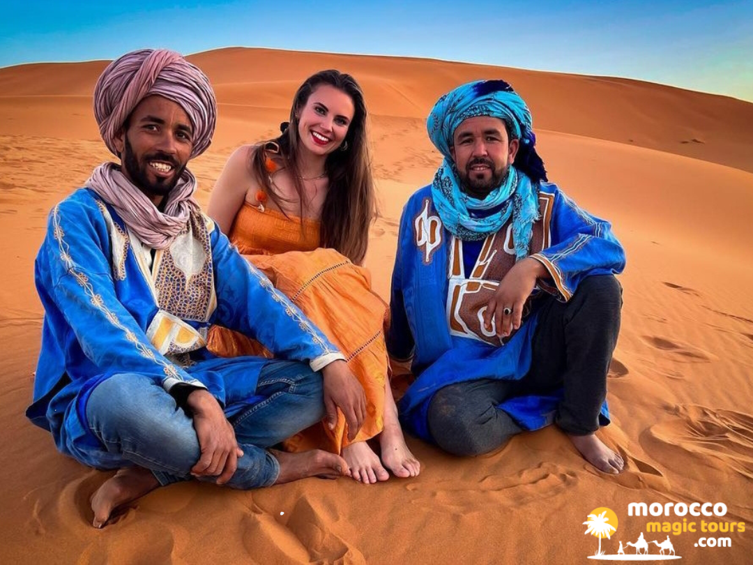 A traveler sitting with local Berber guides on the golden sand dunes during a 3 days tour from fes to Marrakech, the most popular desert tours from Fes.