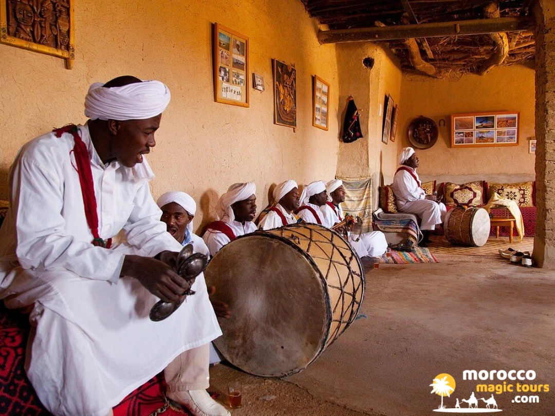 Traditional Gnaoua musicians in white robes and turbans playing large drums and iron castanets in Khamlia village.
