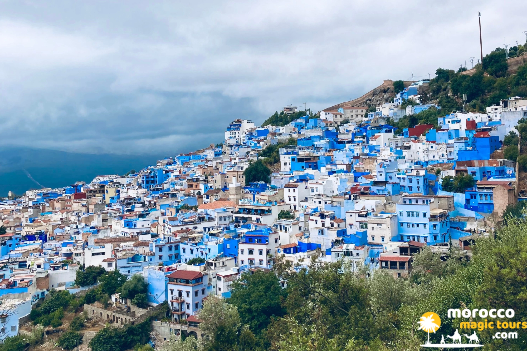 Hillside cityscape view of Chefchaouen blue-washed houses against the Rif Mountains on a 6 days Sahara desert tour from Tangier