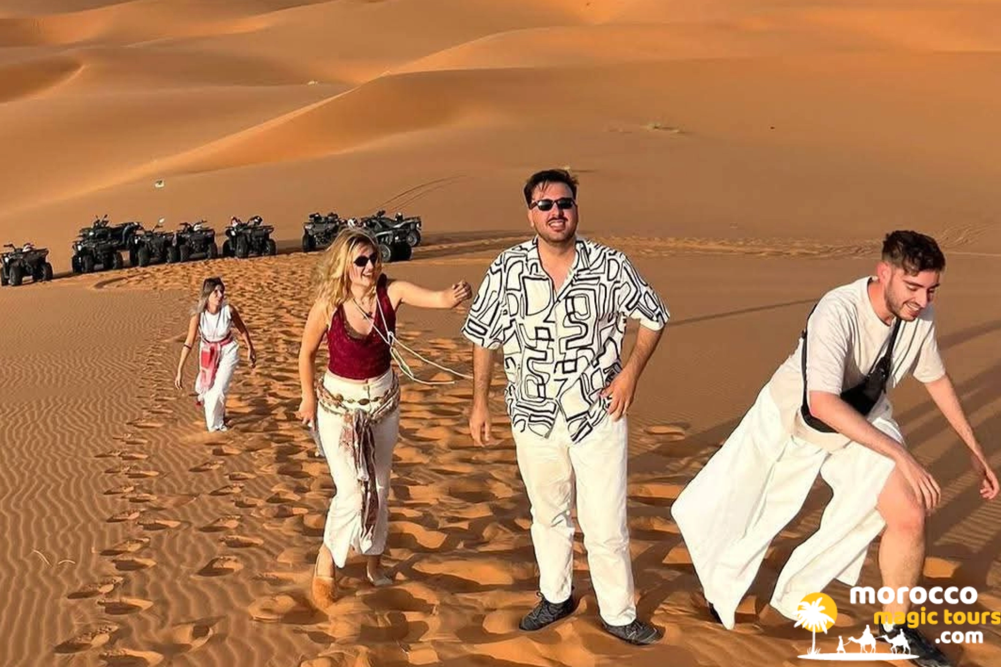 Group of tourists climbing up a steep sand dune with quad bikes parked in the background during a desert tour from Tangier