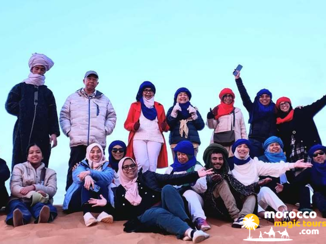 A happy group of international travelers posing together on a sand dune during a 10 days tour from Casablanca.