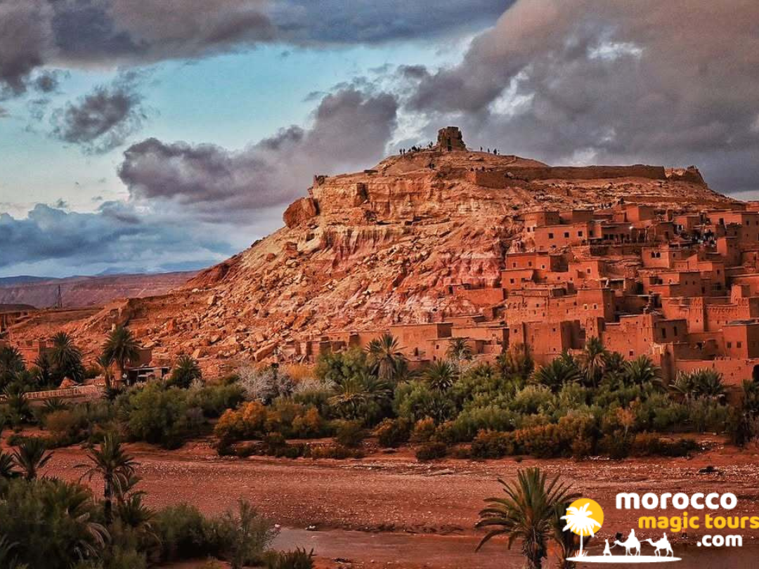 The ancient earthen clay fortress architecture of Ait Benhaddou Kasbah under dramatic striking clouds during a 5 day desert tour from marrakech.
