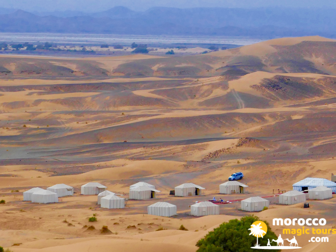 over head view of white tents in rolling sand dunes and desert plains of a luxury desert camp on a premium 5 day desert tour from marrakech