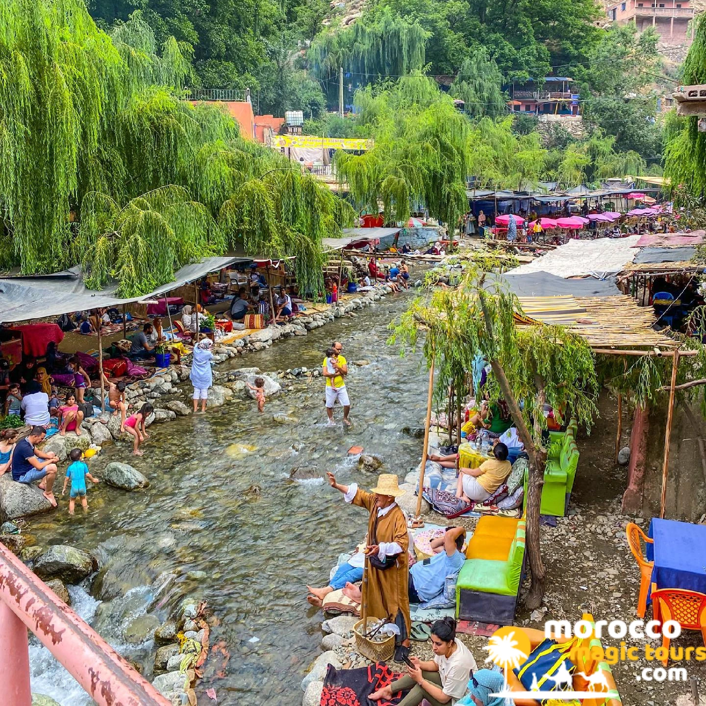 Families wading in the Ourika River beside riverside cushion seating in the Ourika Valley near Marrakech