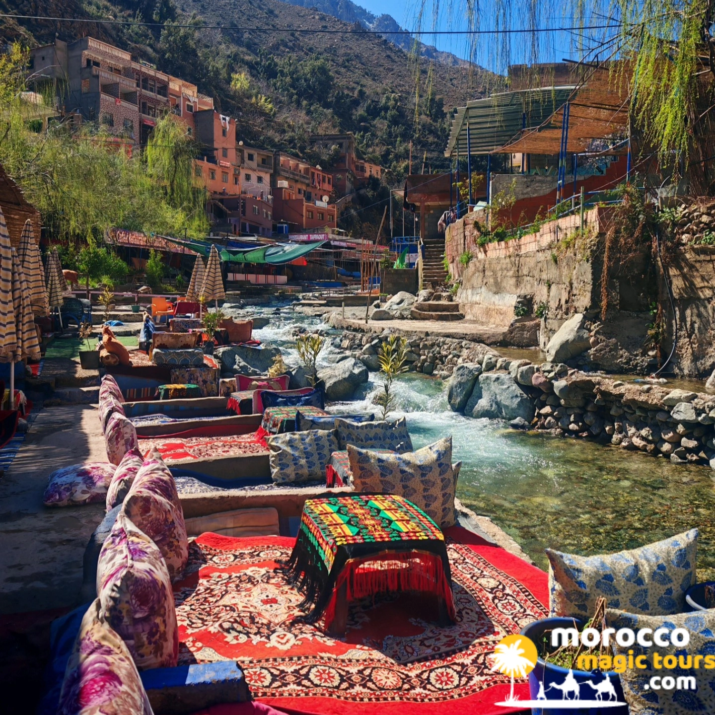 Riverside lounge seating with traditional Berber rugs and cushions beside the Ourika River on a private Marrakech Ourika Valley tour
